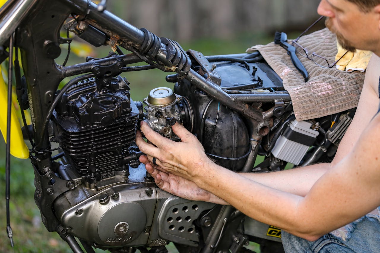 Mechanic repairing a motorcycle engine outdoors, focusing on the carburetor.